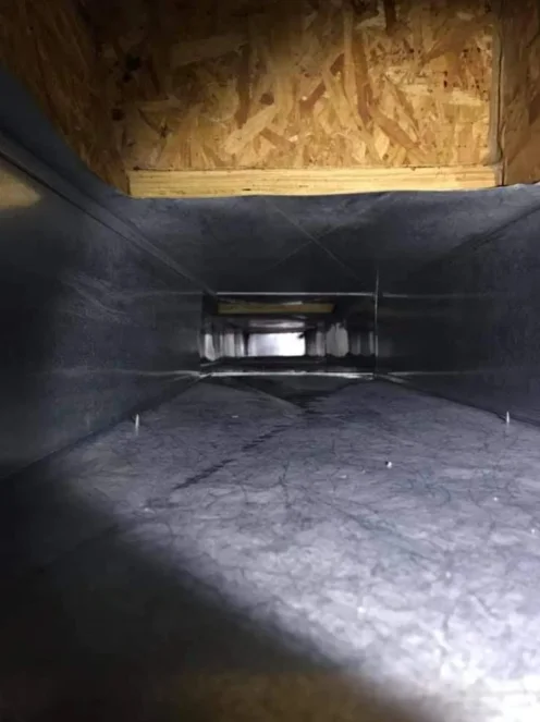 Interior of commercial HVAC duct system with black lining and metal framework during cleaning