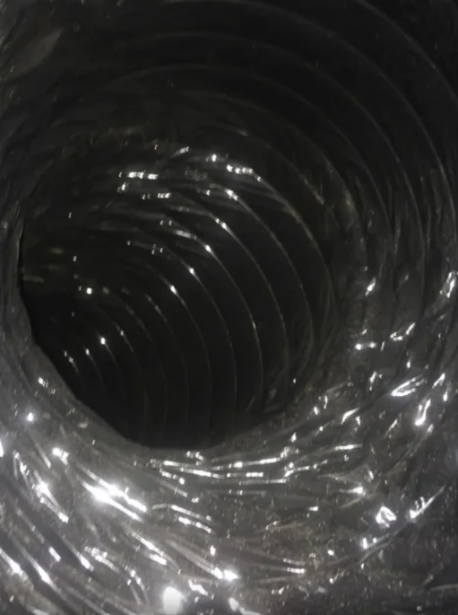 Interior view of metal spiral duct with dust and debris buildup on walls